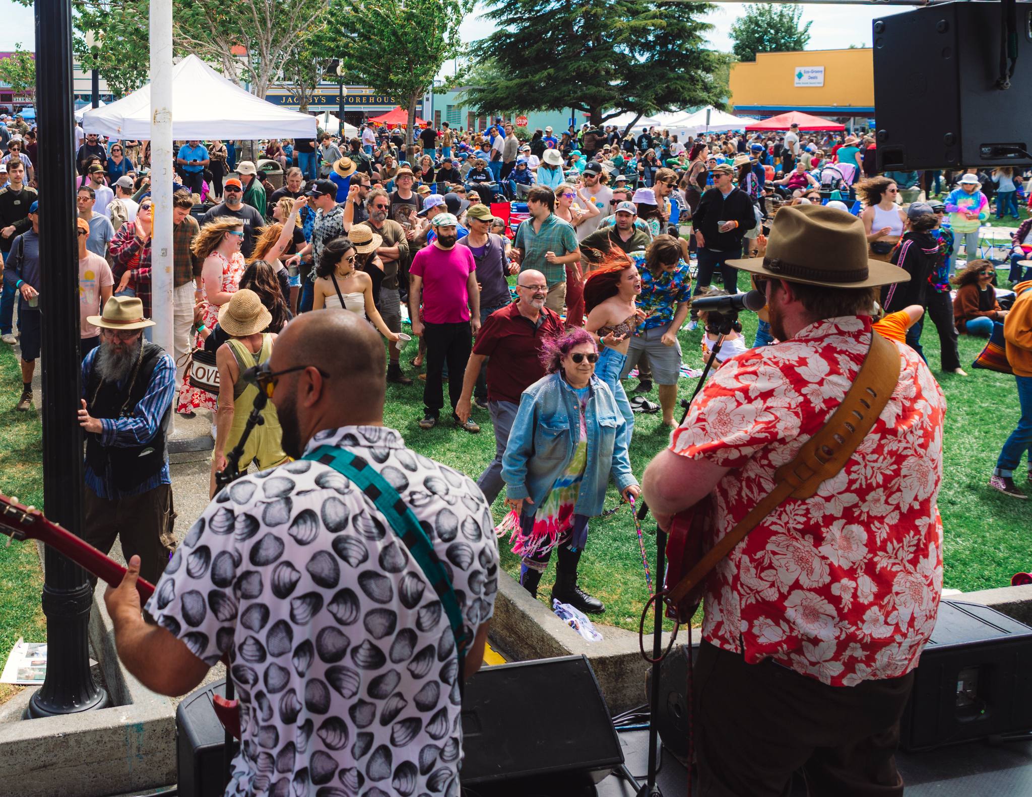 A band is up on stage, looking out onto a crowd of dancing people. The band is two men who are singing into microphones and playing guitars